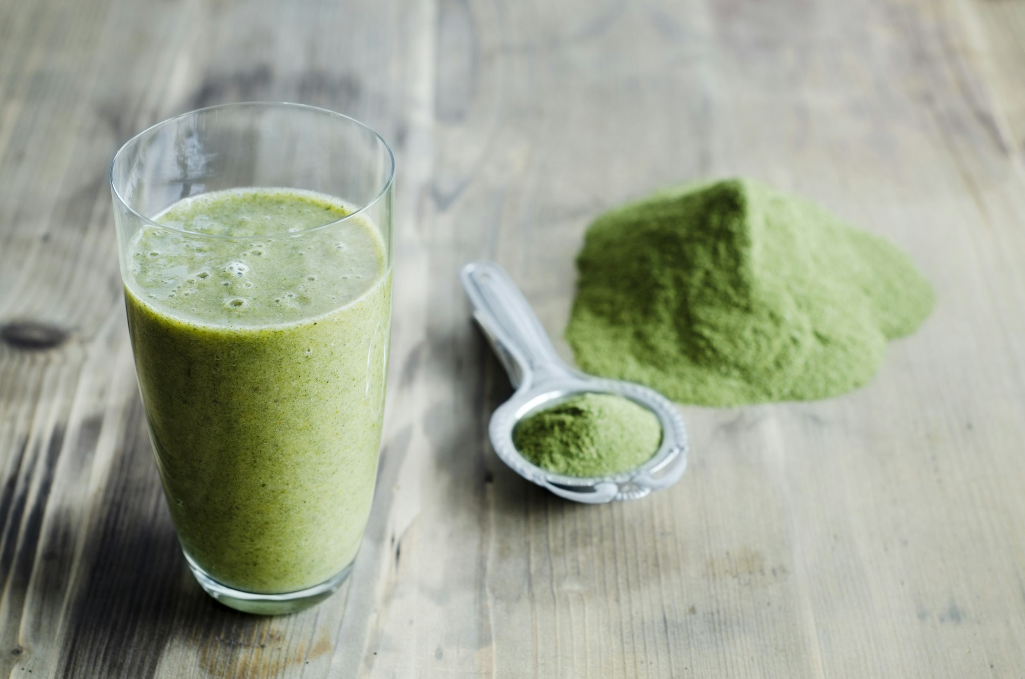 Moringa powder on spoon and wooden table and glass of moringa smoothie