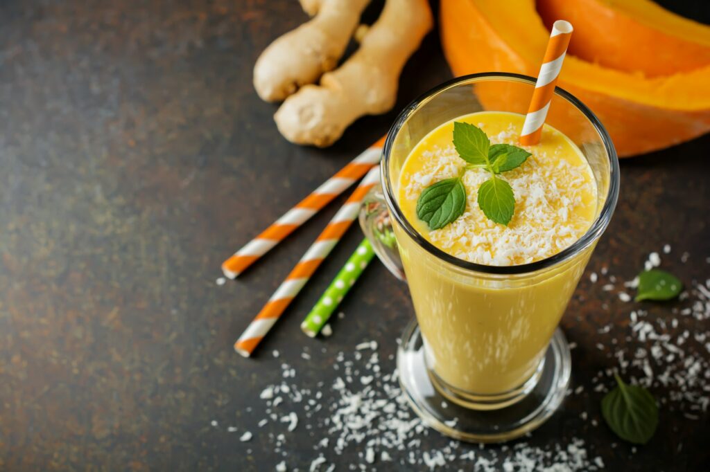 Pumpkin smoothies with ginger and coconut shavings and mint in a glass on a dark stone or concrete b